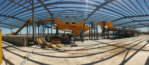 Structure métallique en construction avec des machines jaunes sur un sol en béton sous un ciel bleu.
