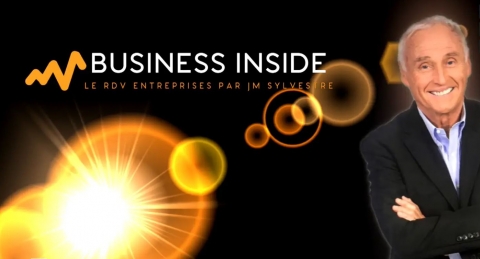 Homme souriant en costume devant un fond noir avec le texte "Business Inside" et des cercles lumineux.